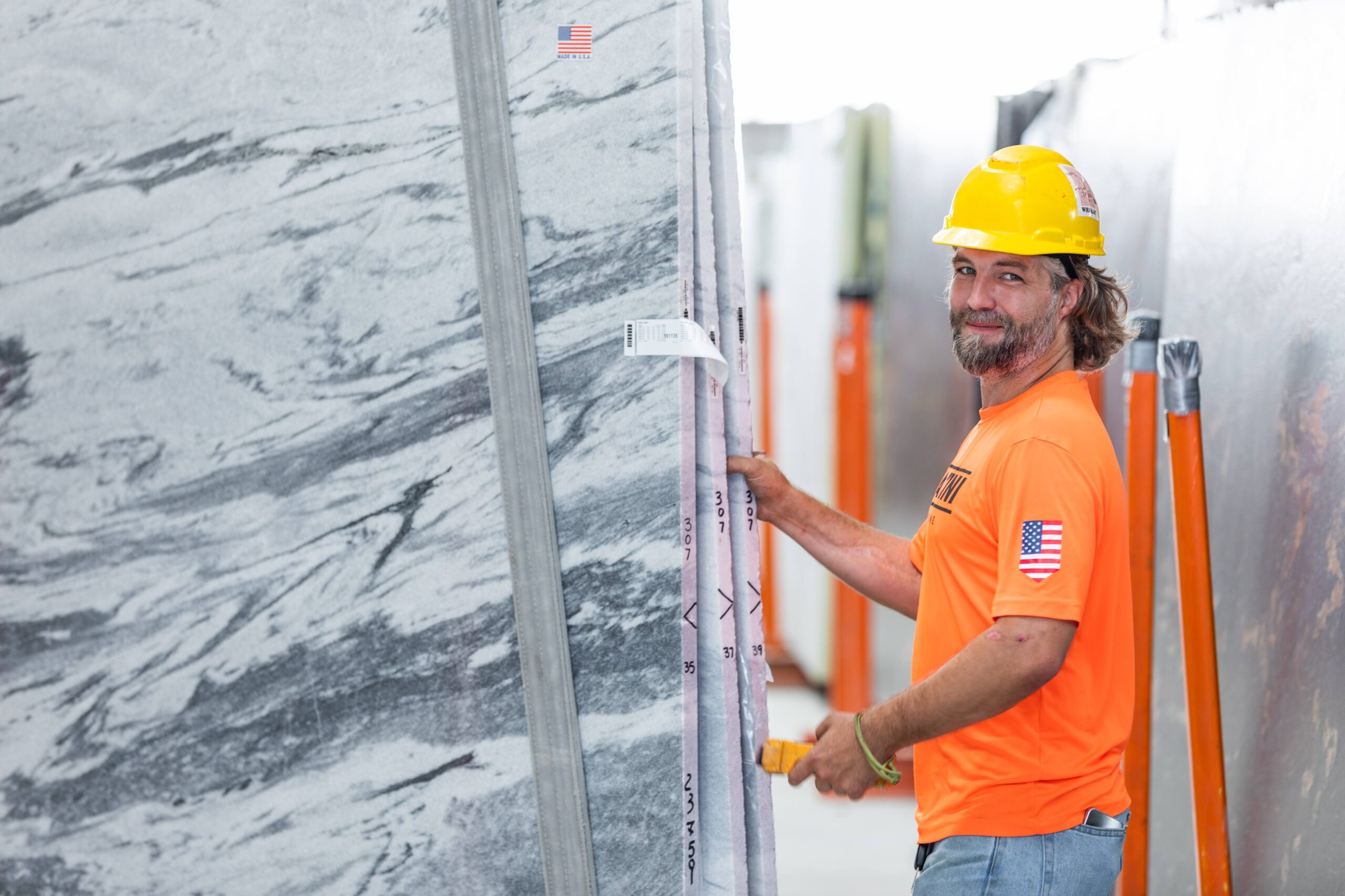 man with yellow hardhat and bright orange shirt with granite slab